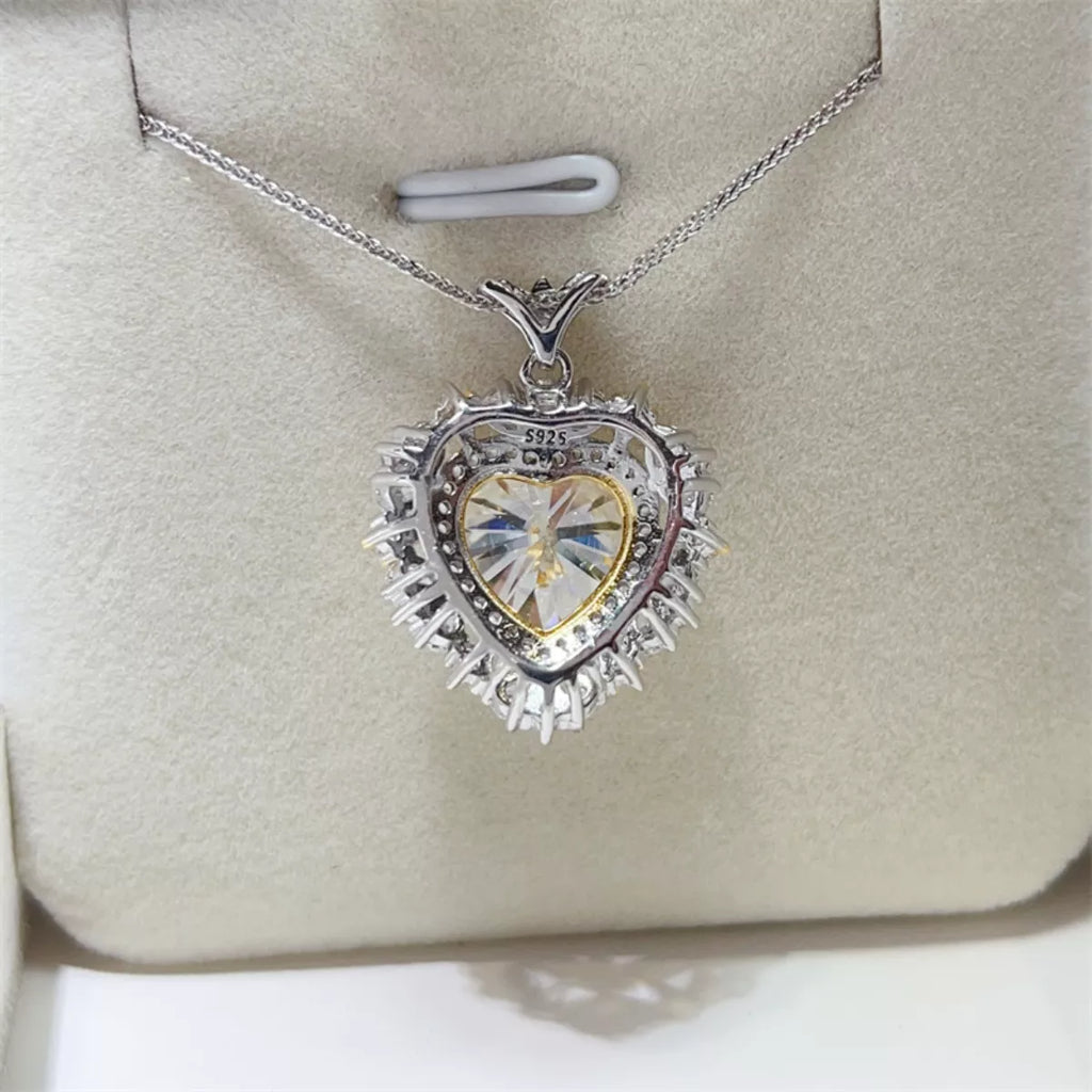 Heart-shaped pendant with a clear gemstone on a silver chain, displayed on a beige cushion.