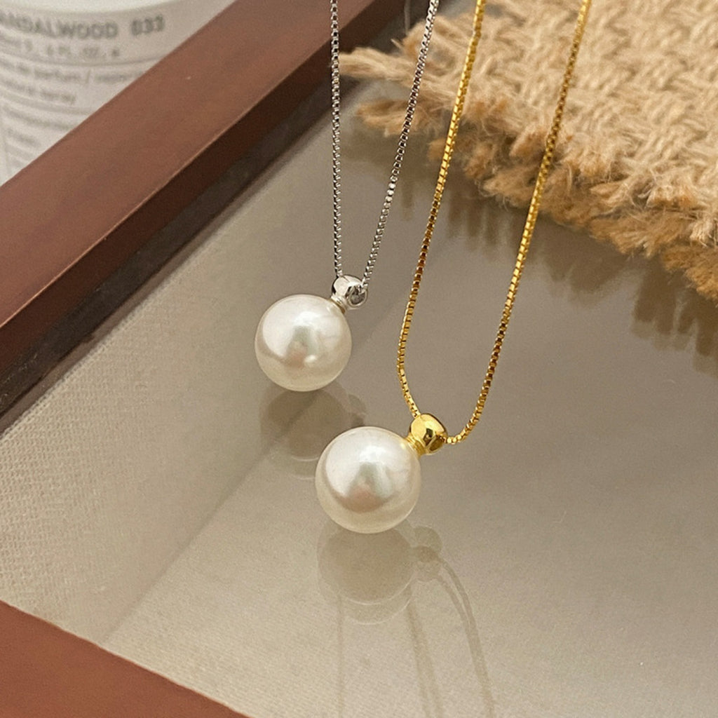 Two pearl necklaces on a textured surface with a book in the background