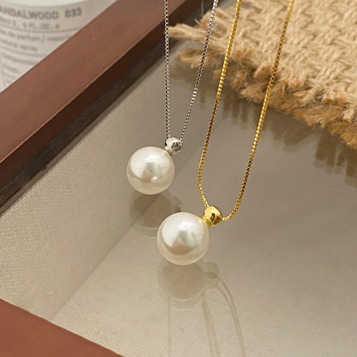 Two pearl necklaces on a textured surface with a book in the background