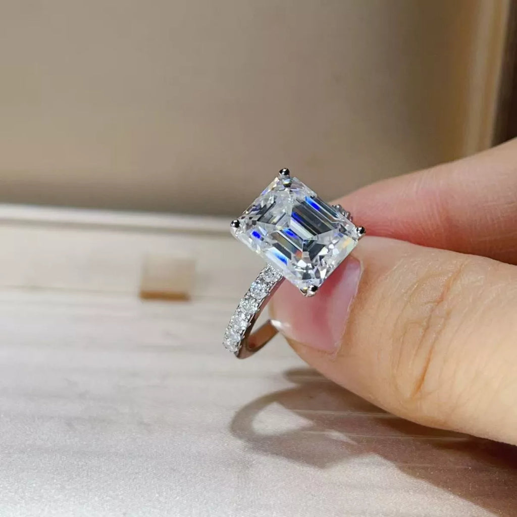 Silver ring with a large diamond held by a hand on a neutral background