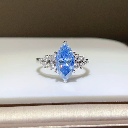 A silver ring featuring a marquise-cut light blue gemstone in the center, flanked by small clear stones on a white display surface.