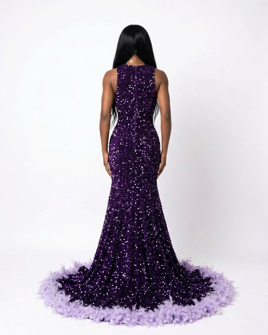 A woman shown from the back wearing a sleeveless, floor-length mermaid gown covered in sparkling purple sequins, with a voluminous feathered or ruffled hem in a pale lavender, against a plain white studio background.