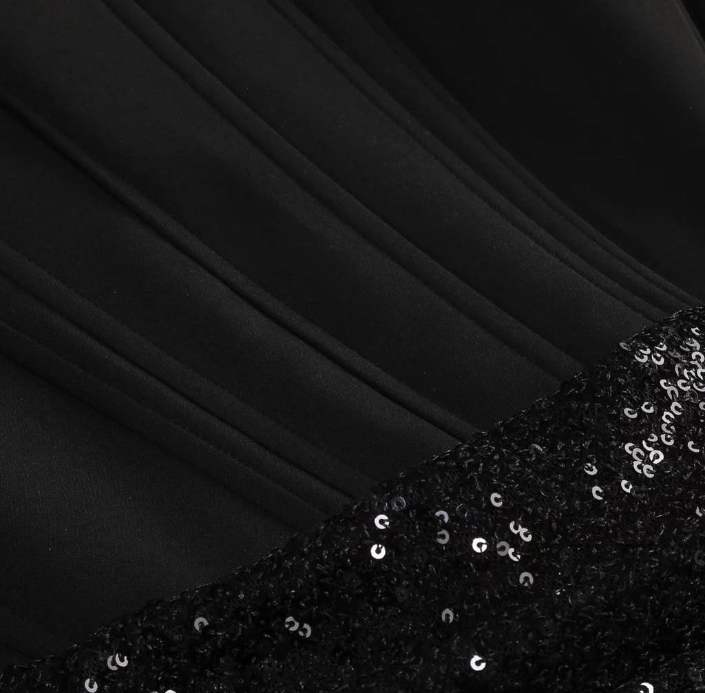 Close-up of a black garment with smooth draped fabric and a contrasting sequined black panel featuring small silver reflective sequins.