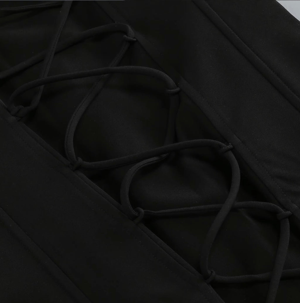 Close-up detail of a black garment featuring a diagonal lacing system with thick adjustable cords threaded through reinforced eyelets.