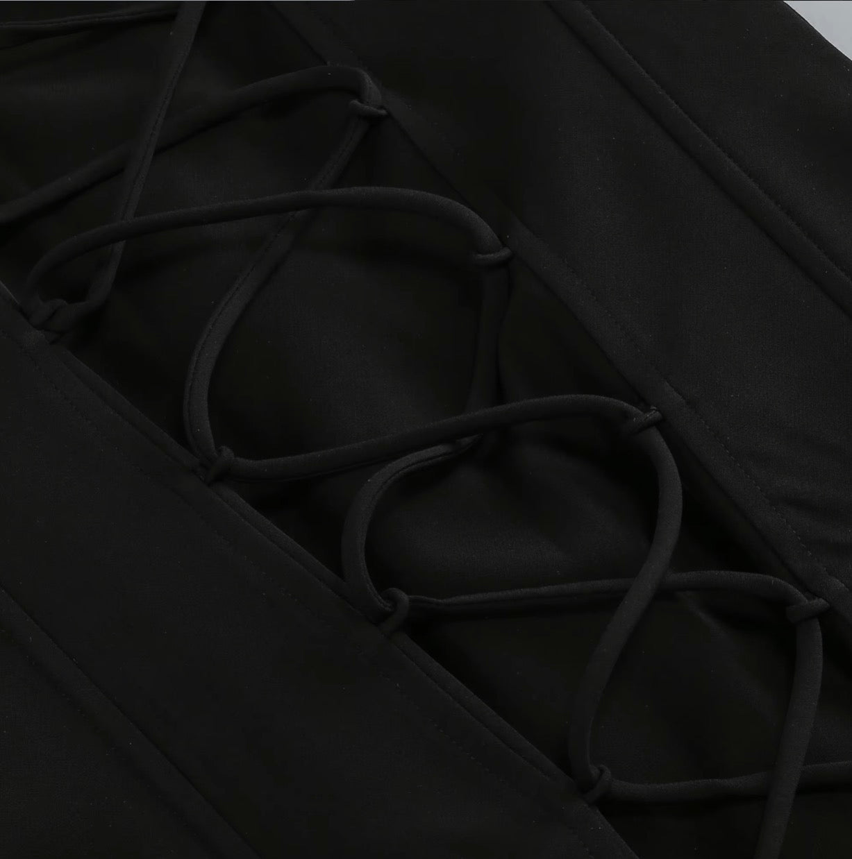 Close-up detail of a black garment featuring a diagonal lacing system with thick adjustable cords threaded through reinforced eyelets.