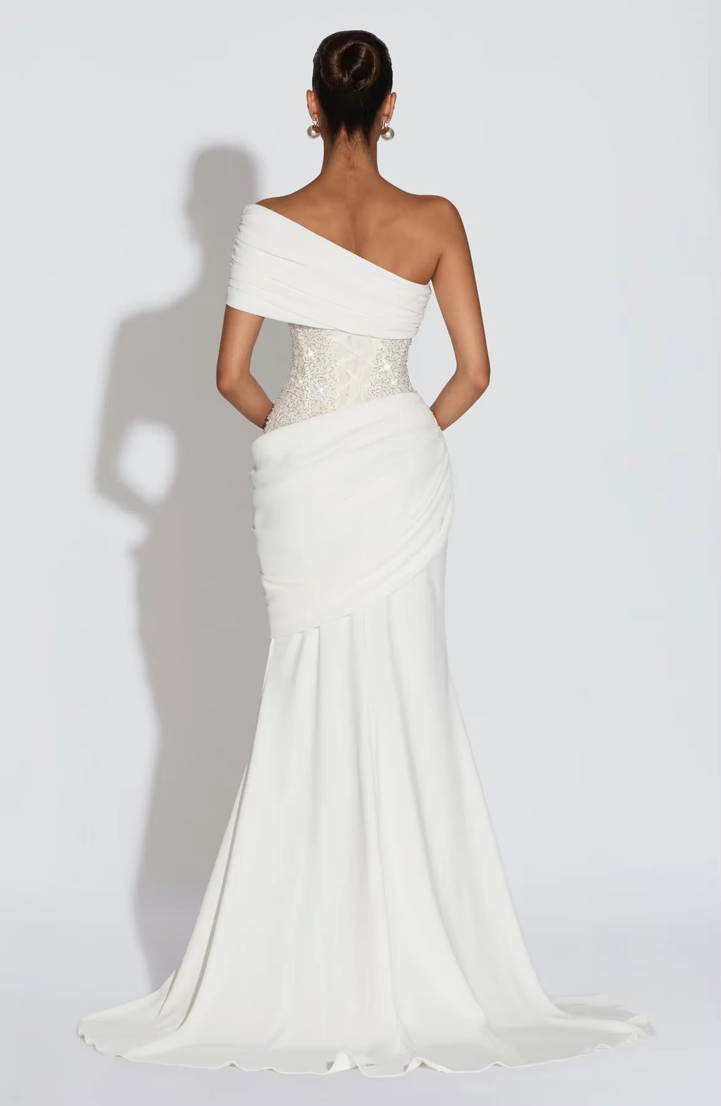 White one-shoulder gown with beaded details on a plain background