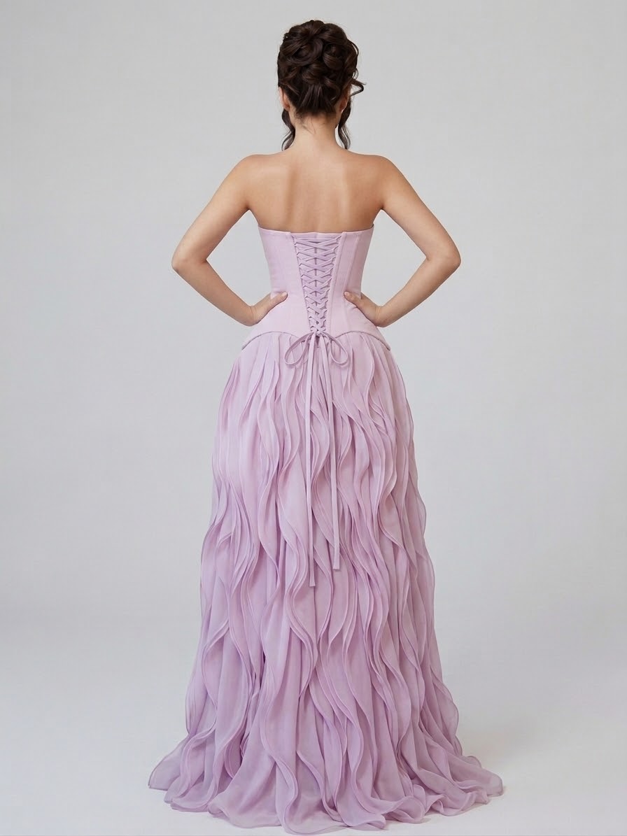 A woman shown from the back wearing a strapless formal gown in a soft light purple/lilac color. The dress has a structured corset-style bodice with lace-up detailing and a voluminous, layered ruffle skirt. BY KONFIDENTIAL KOUTURE