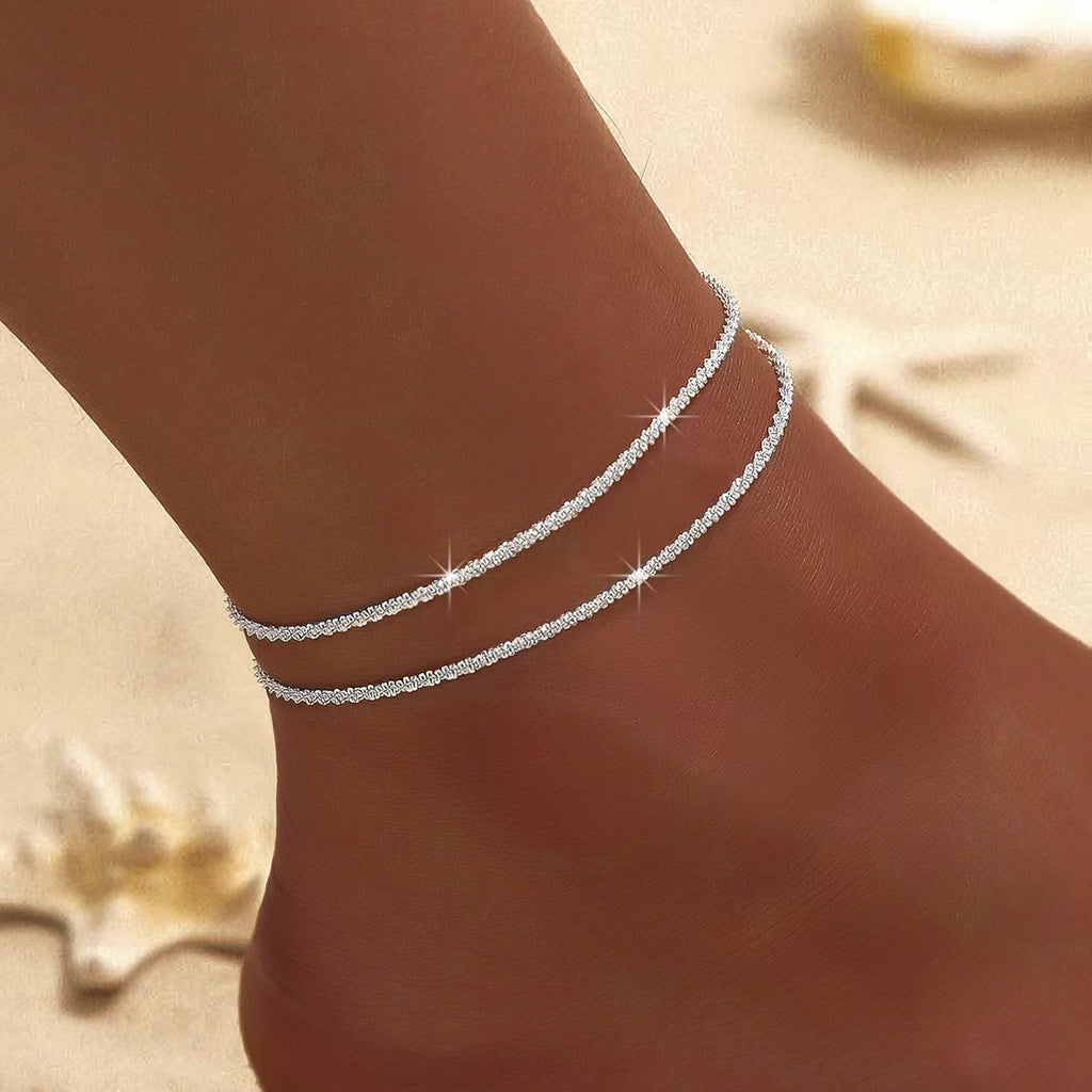 Silver anklets on a person's ankle against a blurred background
