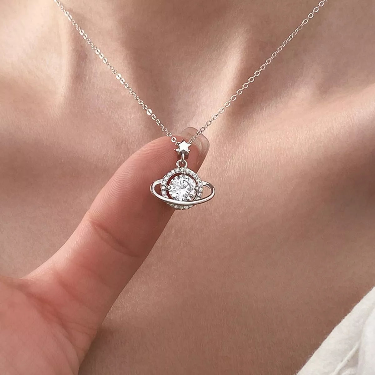 Silver necklace with a pendant held by a finger against a neutral background