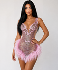 A woman modeling a pink and silver beaded mini dress with feather trim against a plain light gray background.