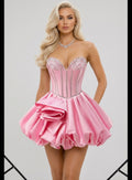 A blonde model wearing a pink strapless mini dress with a corset-style bodice, silver rhinestone trim, and a ruffled tiered skirt, photographed against a light gray studio background.
